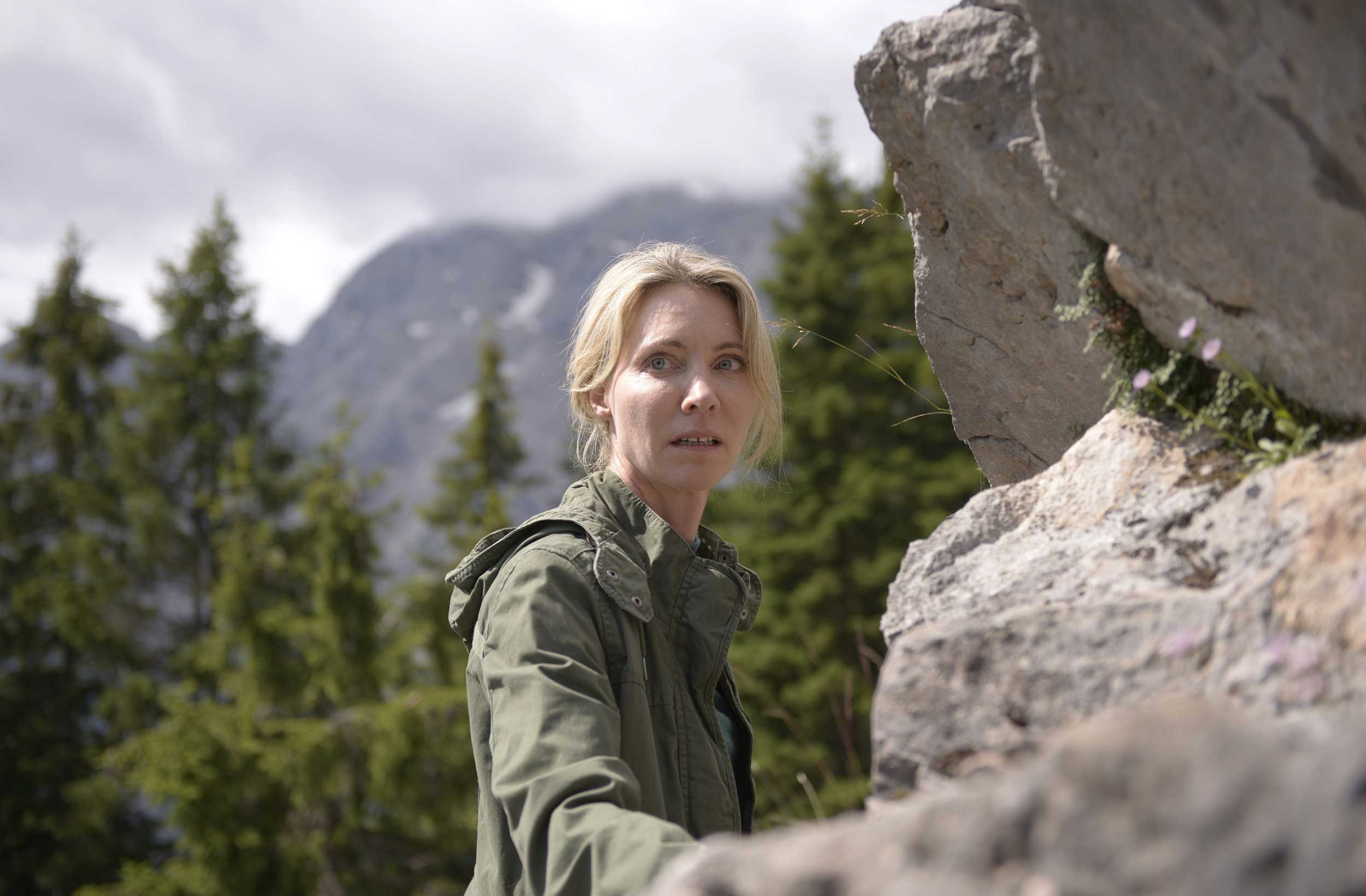 eine Frau steht in den Bergen an einer Felswand und guckt erschrocken