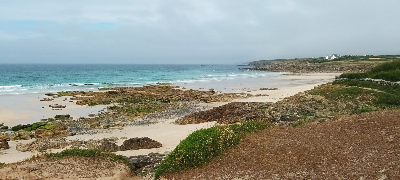 Sandiger Strand umgeben von grüner Küstenlandschaft